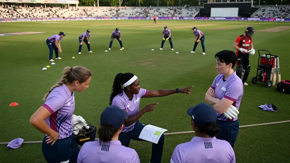 Medium tactical view of fielders set on a green outfield as a bowler runs in during a women's short-format match
